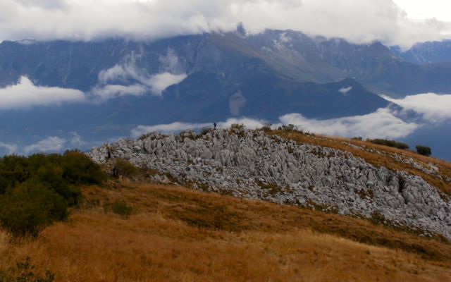 Caminante en un afloramiento rocoso con los Alpes Julianos al fondo.