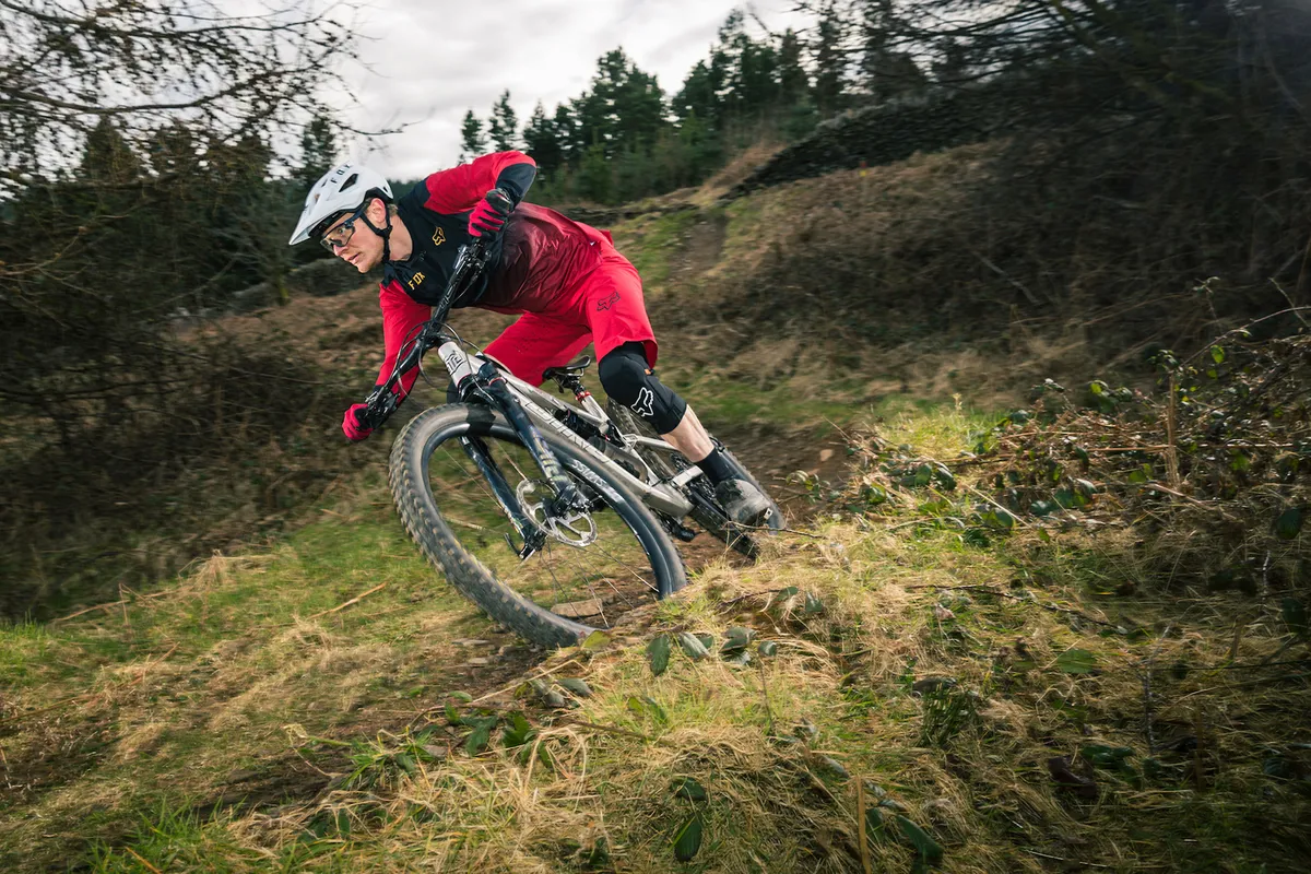 Ćter de pĆ”jaro 9 Ciclista en rojo y negro montando la bicicleta de montaƱa con suspensión total Bird Aether 9 cuesta abajo