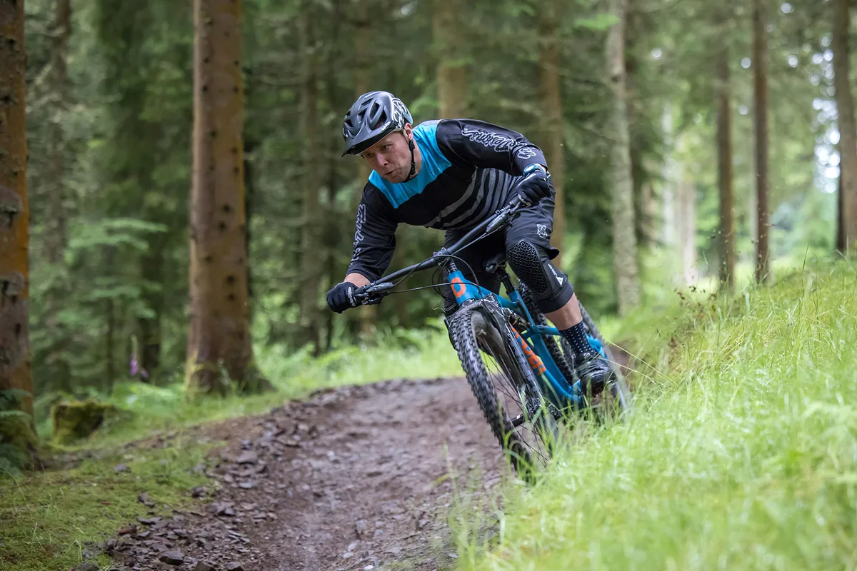 Ciclista masculino vestido de azul montando la bicicleta de montaña Sonder Evol GX Eagle a través del bosque