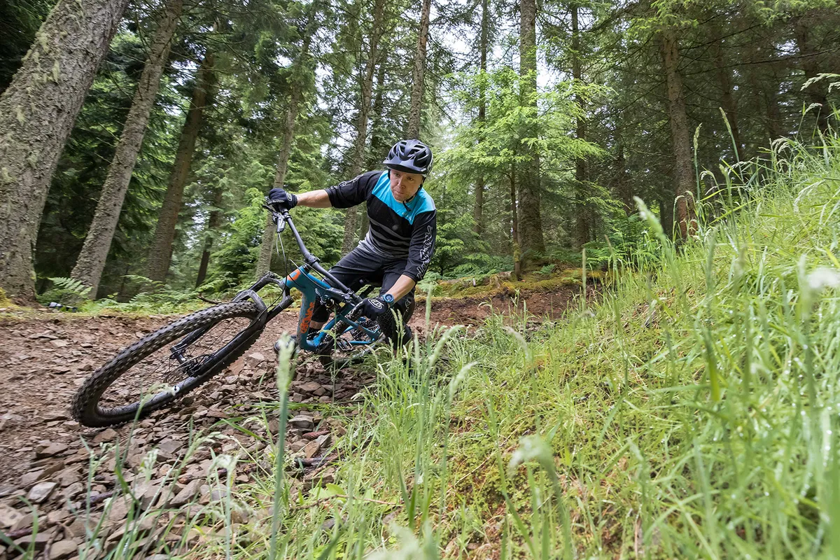 Ciclista masculino vestido de azul montando la bicicleta de montaña Sonder Evol GX Eagle a través del bosque
